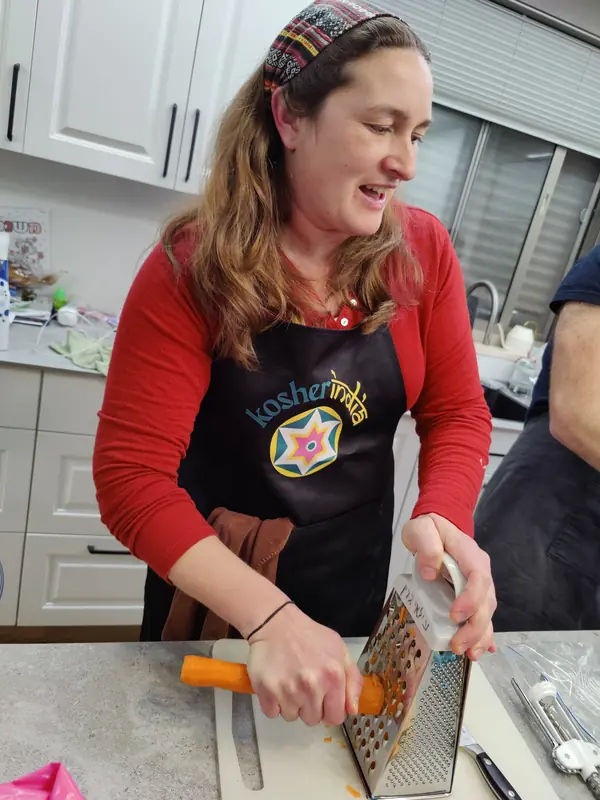 A smiling guest grating carrots in a Kosher India apron